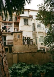 Buildings with balconies and plants viewed from below.